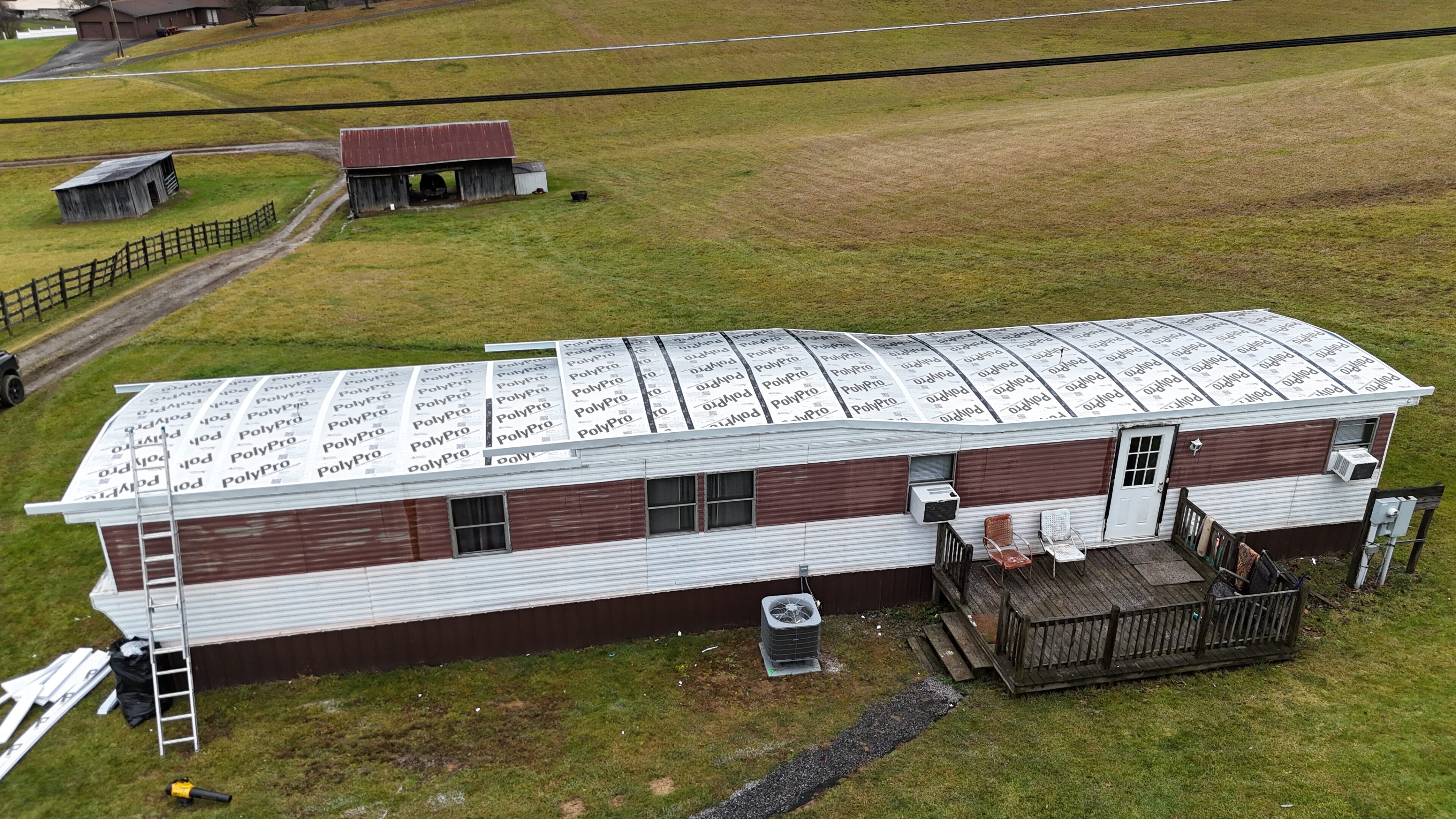 Aerial view of a long white building with a metal roof in a grassy field.
