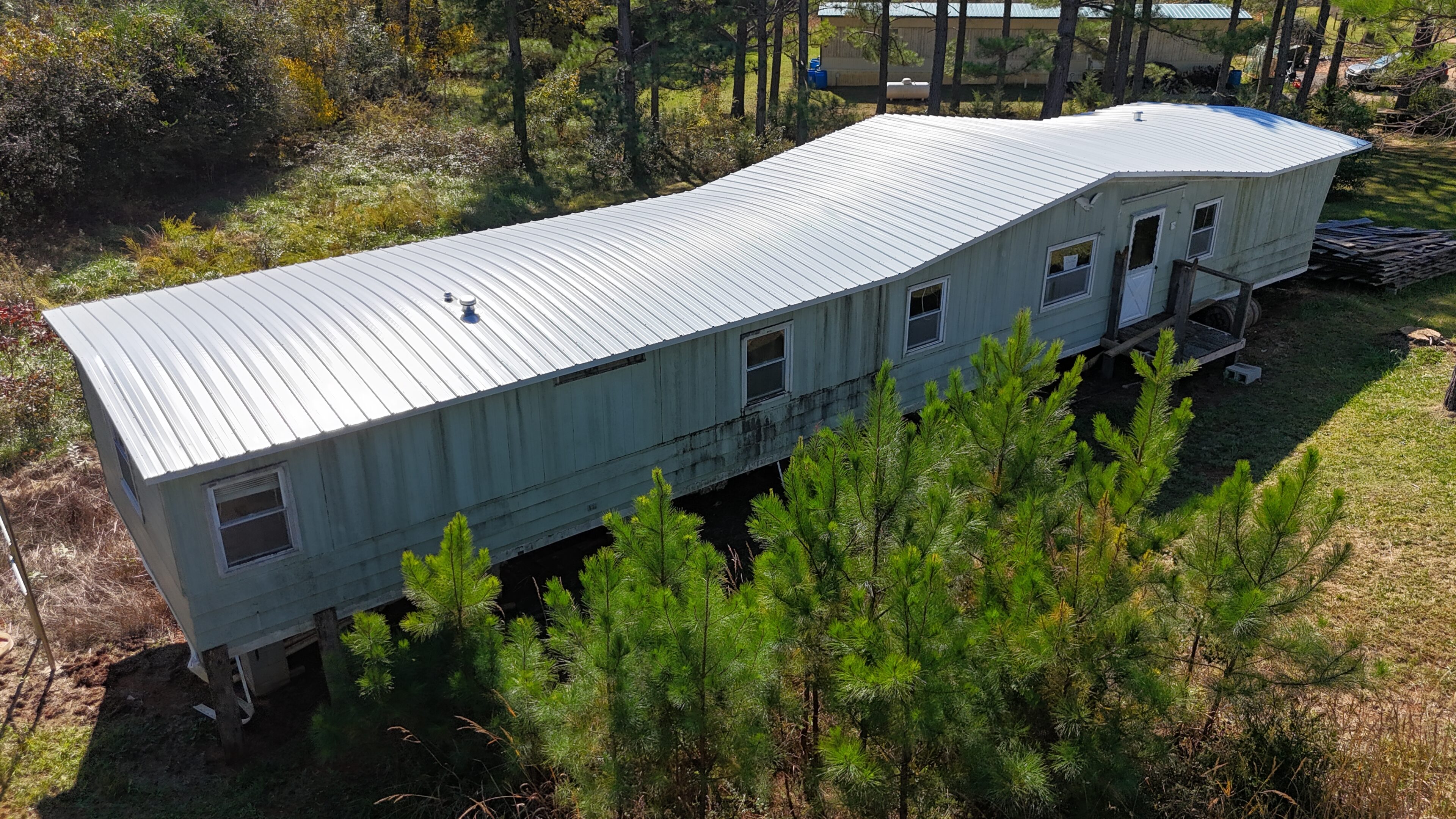A white mobile home surrounded by trees in a wooded area.