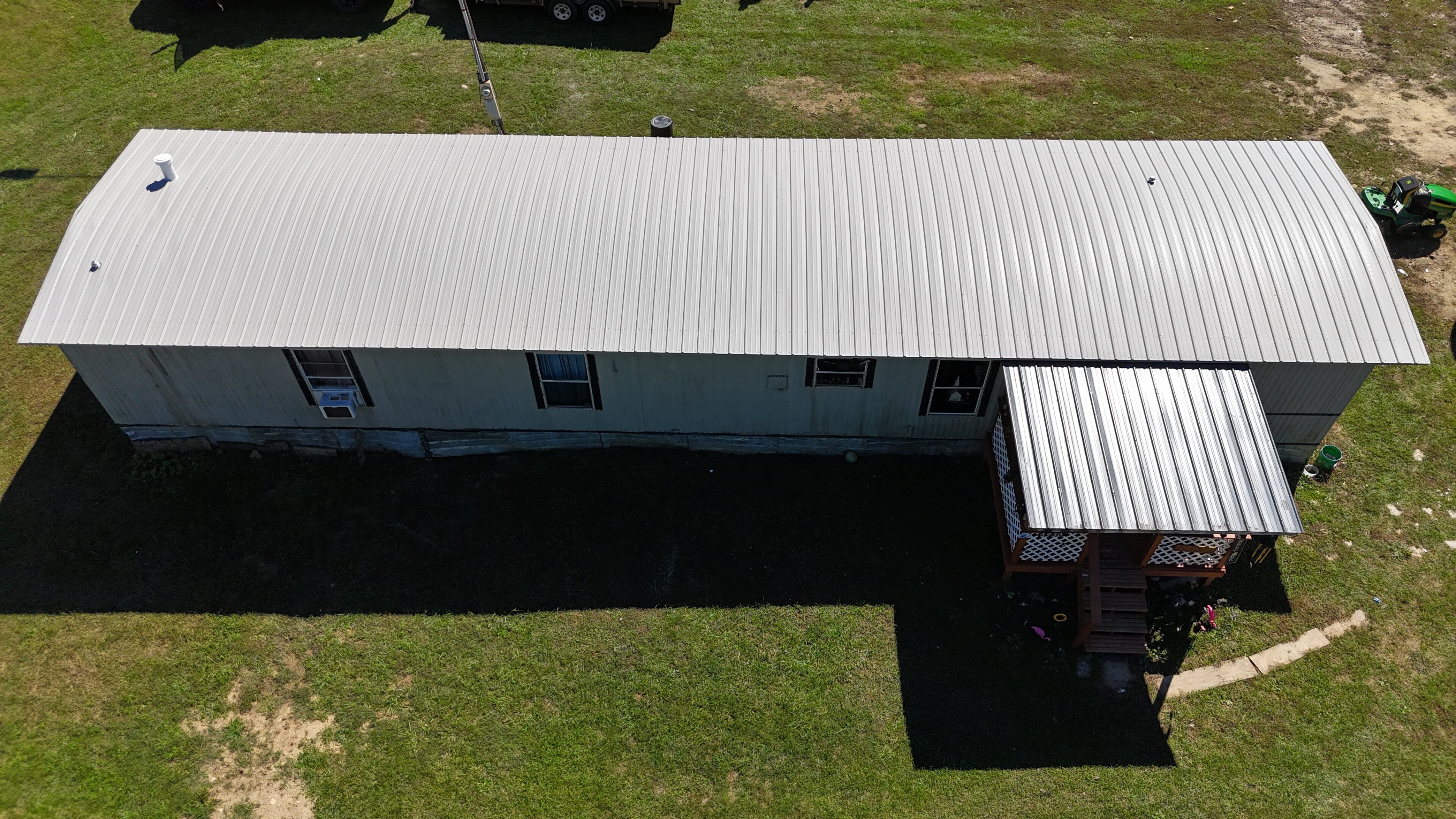 A white building with a metal roof casting a shadow on the grass.