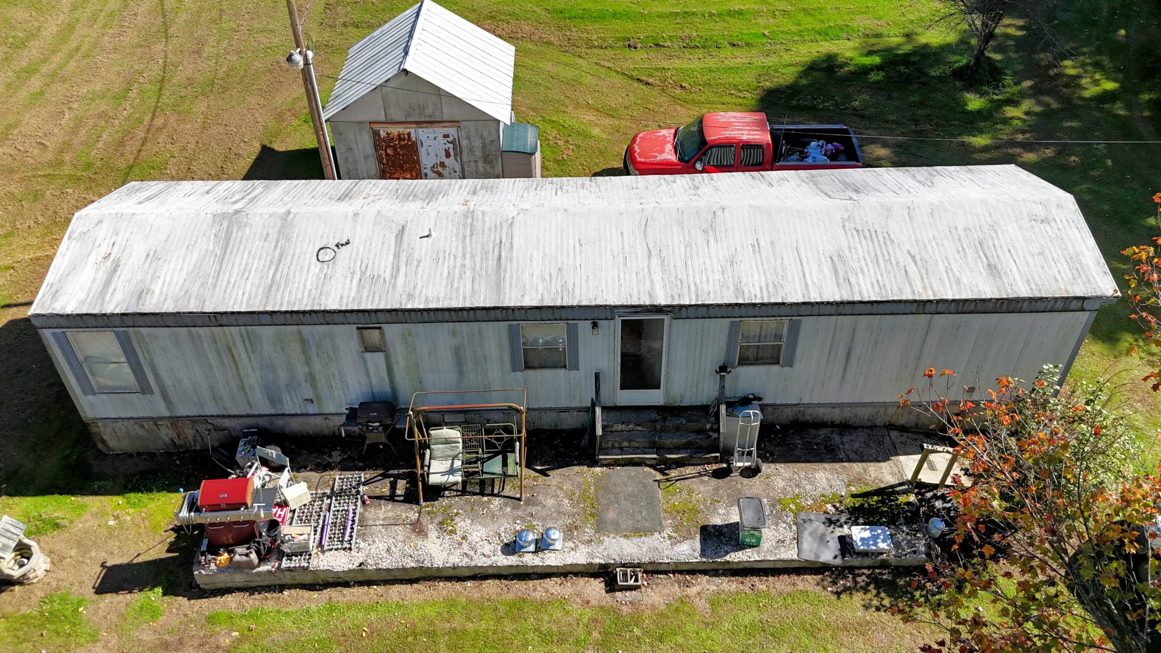 Aerial view of a mobile home with a metal roof and vehicles parked nearby.
